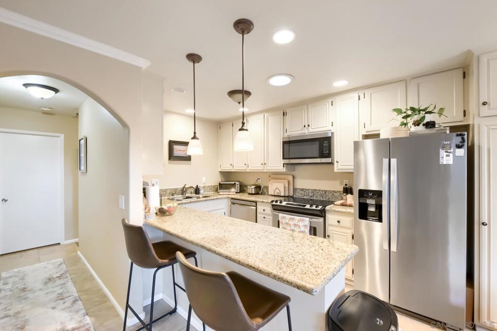 Remodeled kitchen at 4339 Caminito Del Diamante #60 with a granite breakfast peninsula, two leather counter stools, white shaker cabinets, stainless steel appliances, and pendant lights