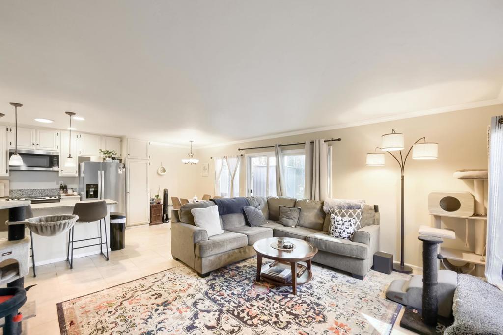 Living room with a gray sectional and patterned area rug over tile, looking toward the kitchen breakfast bar and a sliding door to the patio
