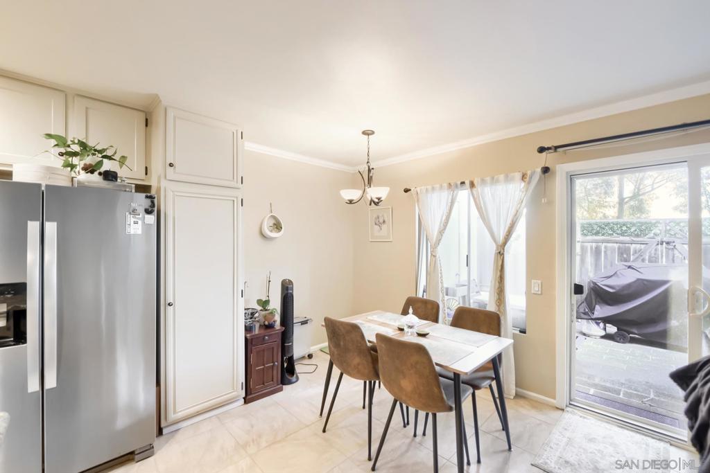 Dining area with a stainless refrigerator and white cabinets beside a sliding glass door that opens to the patio and greenery