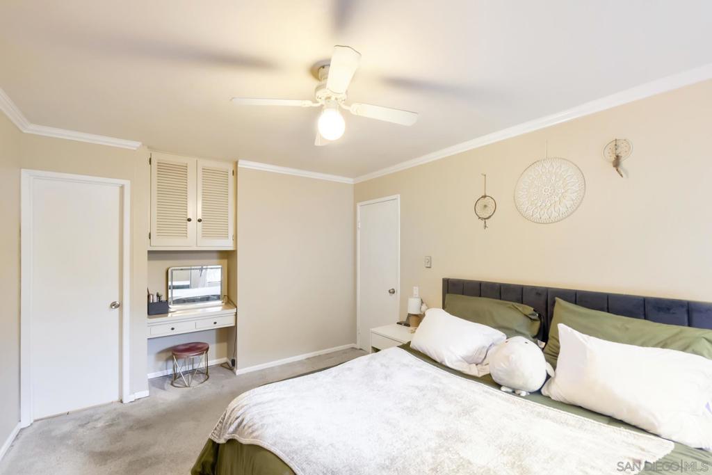 Primary bedroom with a dark upholstered headboard, green bedding, a built-in vanity desk with cabinets above, ceiling fan, and carpet