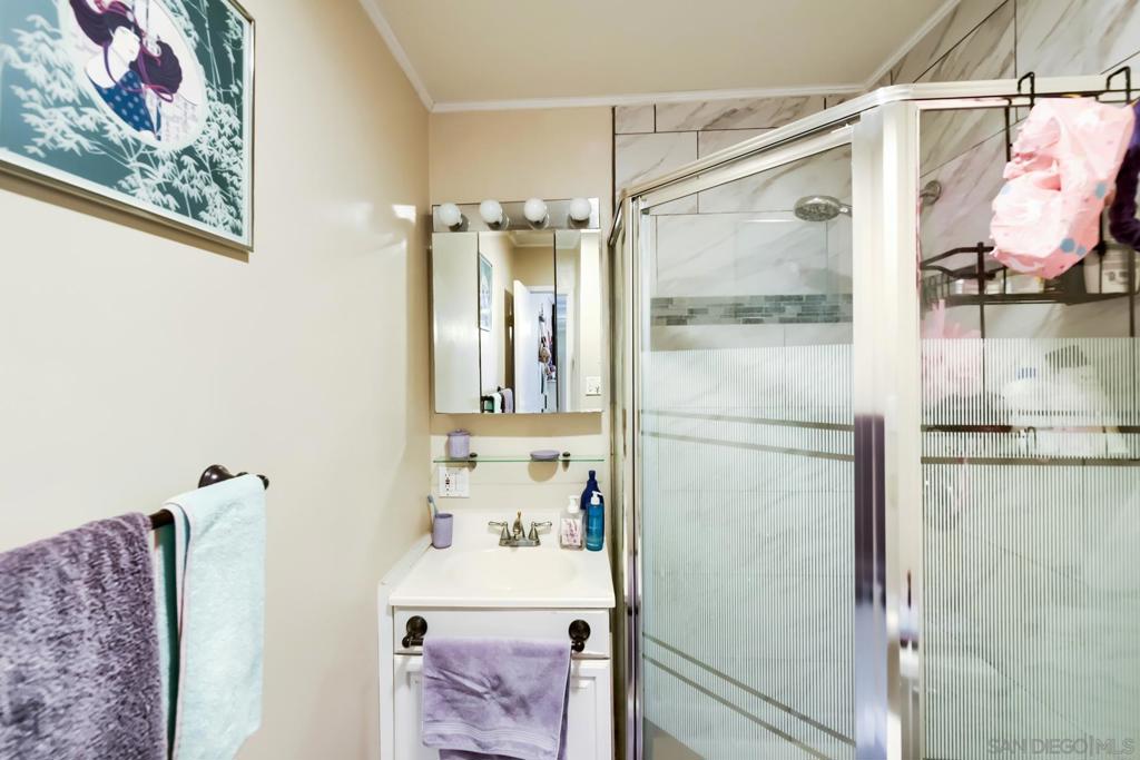 Remodeled bathroom with marble-look tile walls, a framed-glass walk-in shower, a framed vanity mirror with a four-bulb light bar, and a white vanity