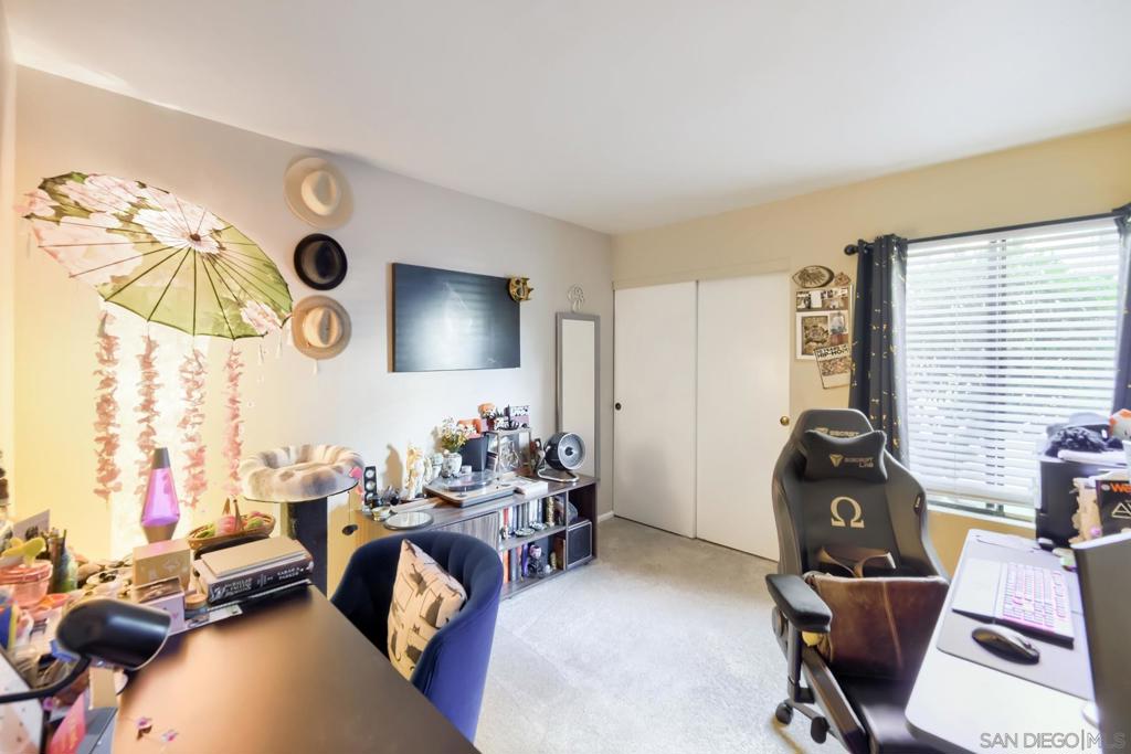 Second bedroom used as a home office and den, with a desk, a gaming chair, a sliding-door closet, and a bright window over carpet